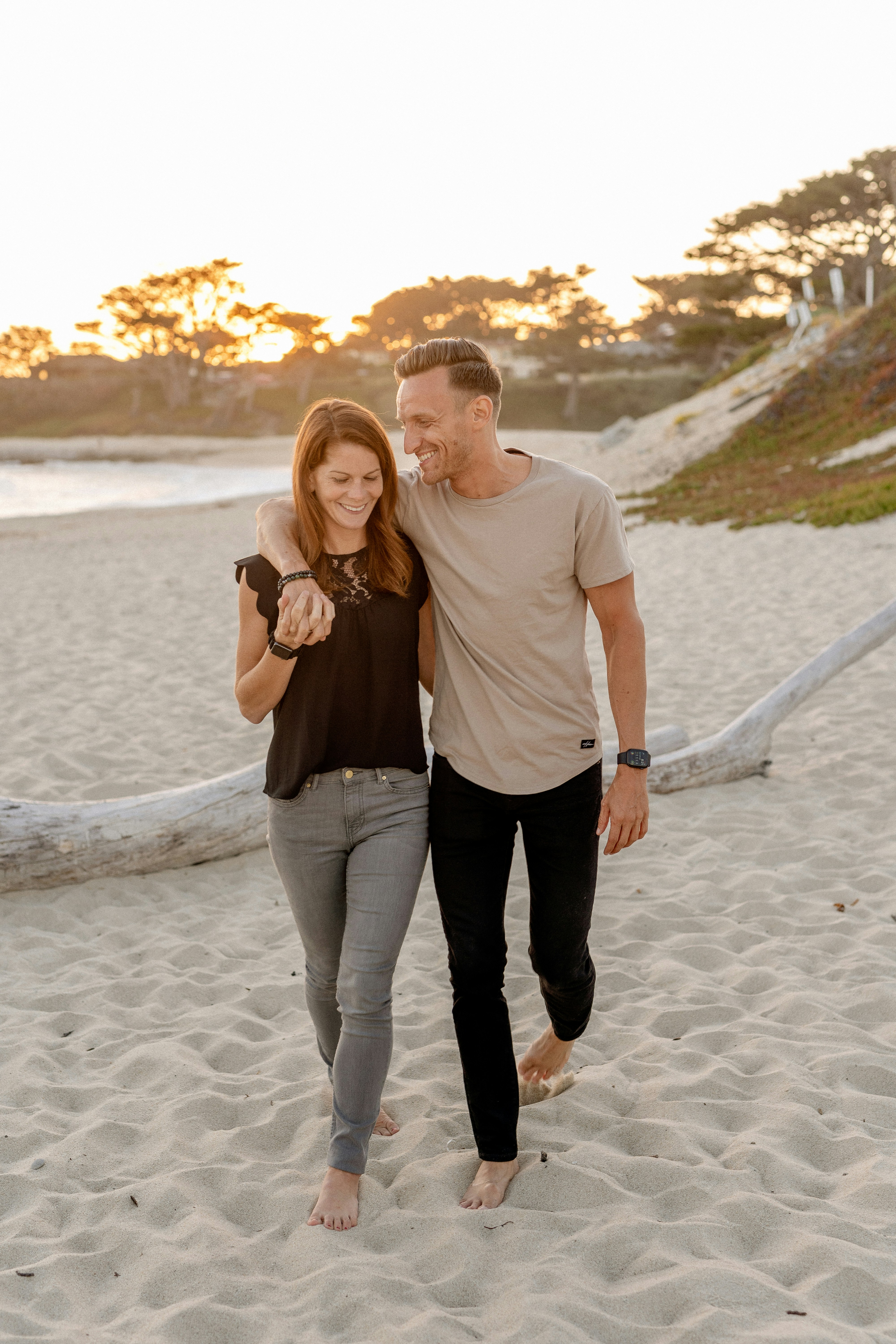 A happy married couple walking barefoot on a sandy beach at sunset, holding hands and laughing together to illustrate healthy communication, quality time, and how to romance your spouse.